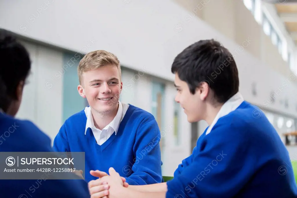 Three male students wearing blue school uniforms talking in corridor
