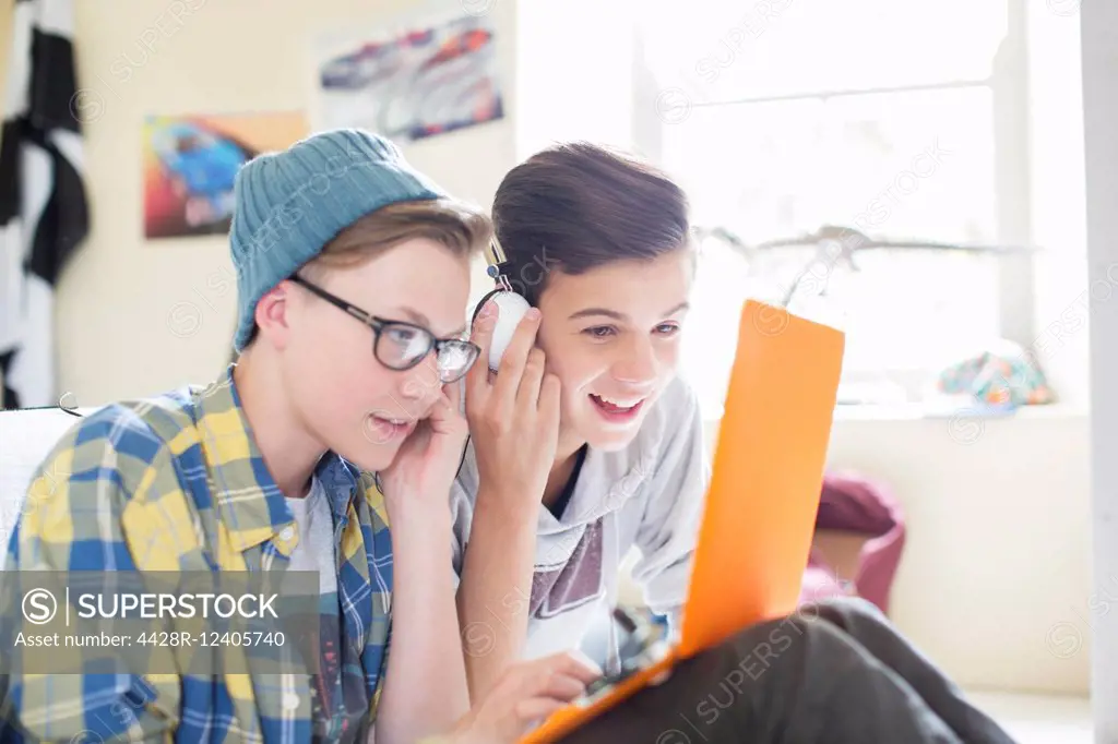 Two teenage boys sharing laptop and headphones in room