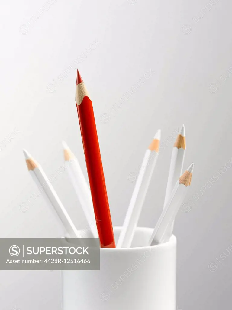 Tall red pencil in cup with smaller white pencils still life