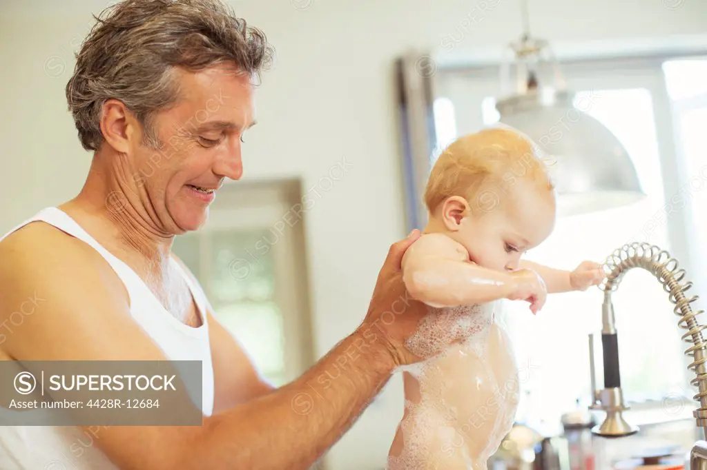 Father washing baby in kitchen sink, London, UK