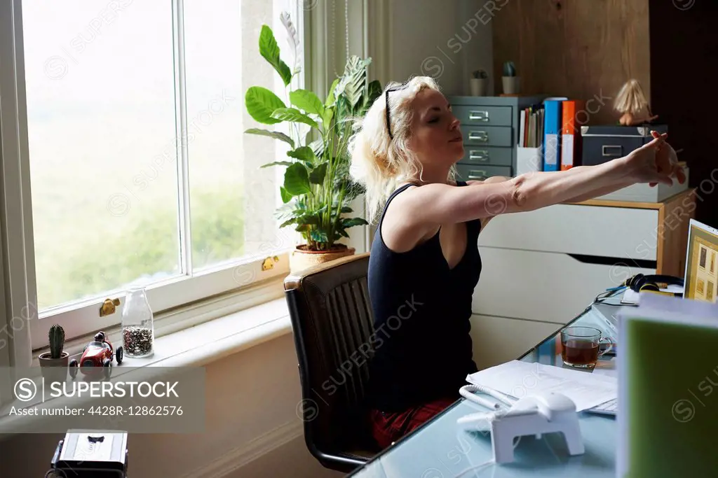 Young woman stretching arms at desk in home office