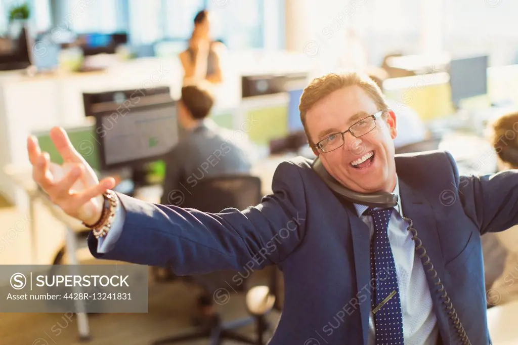 Portrait of exuberant businessman with arms outstretched talking on telephone