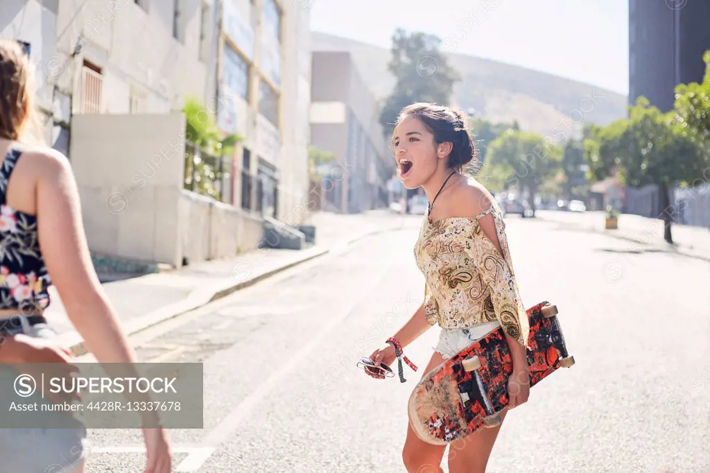 Teenage girl with skateboard on sunny urban street