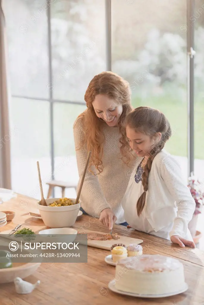 Pregnant mother and daughter preparing food at dining table