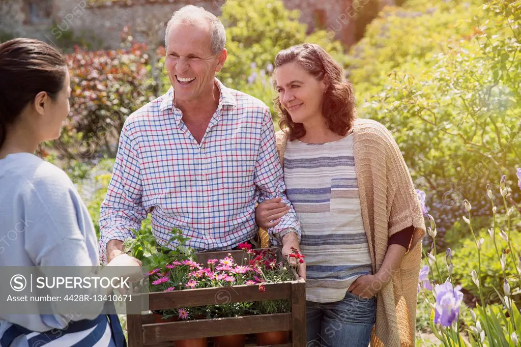 Plant nursery worker helping smiling couple with flowers in garden