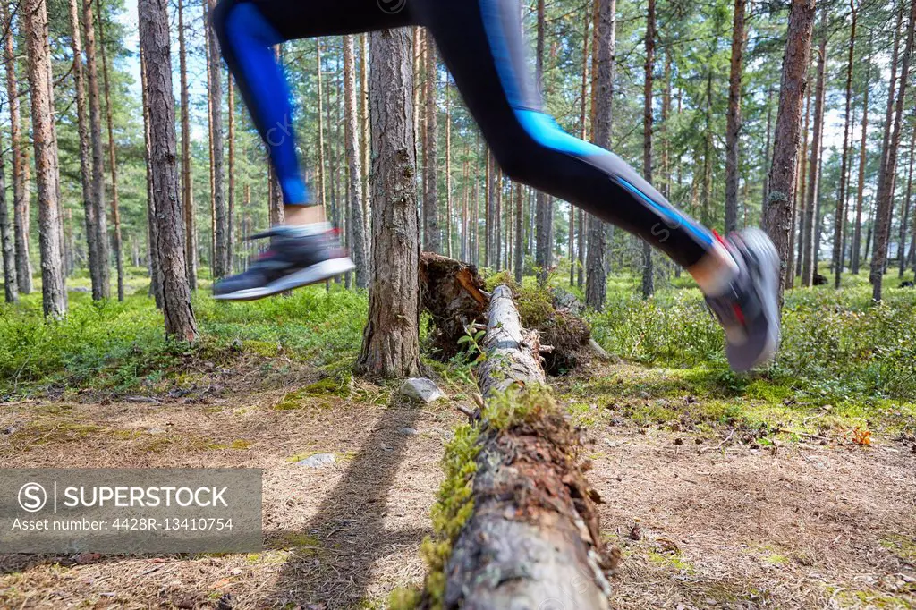 Runner jumping over fallen log on trail in woods