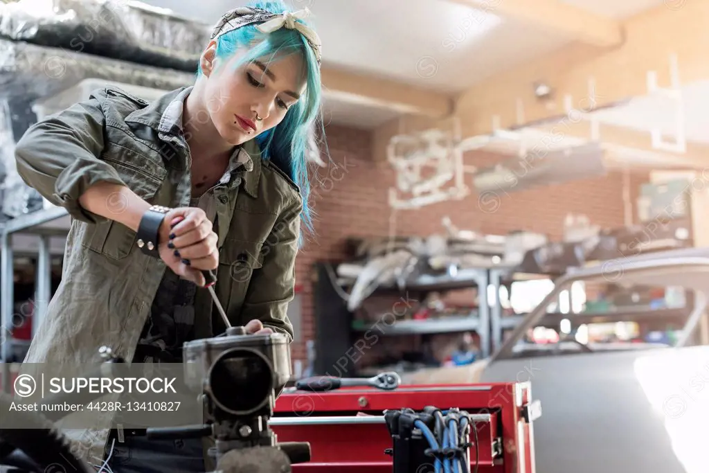 Young female mechanic with blue hair repairing part in auto repair shop