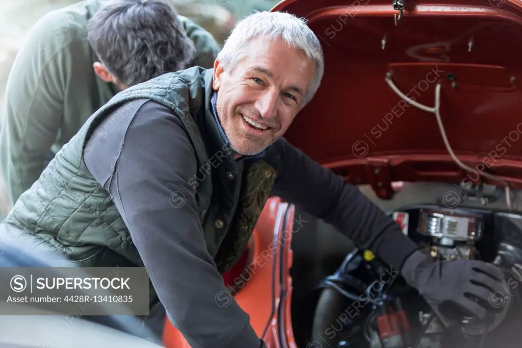 Portrait smiling mechanic fixing engine in auto repair shop