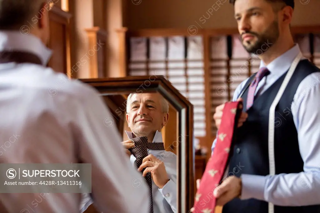 Tailor showing ties to businessman at mirror in menswear shop