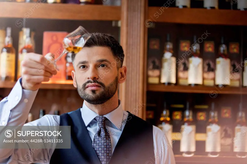 Serious well-dressed bartender examining whiskey