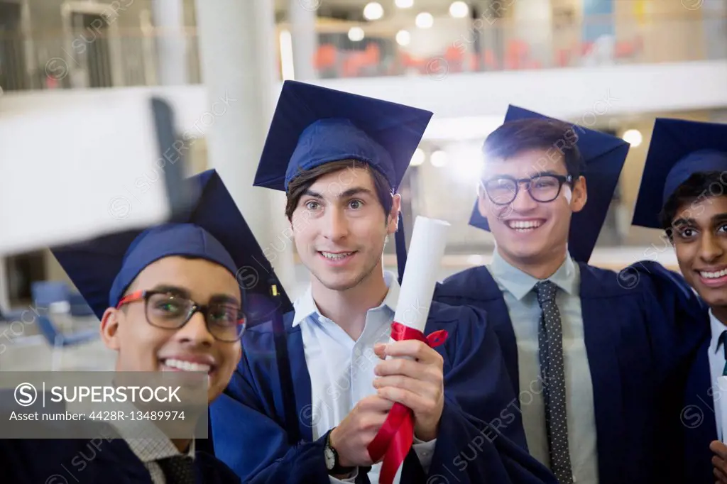 Male college graduates in cap and gown with diploma taking selfie