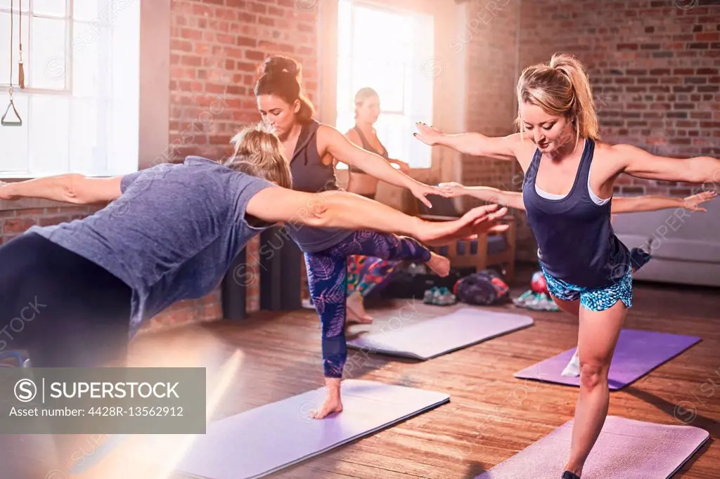 Women practicing yoga warrior 3 pose in exercise class gym studio