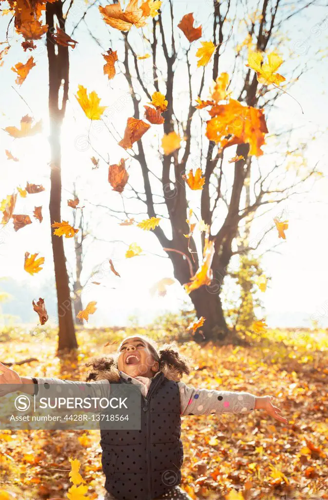 Playful girl throwing leaves overhead in sunny autumn park