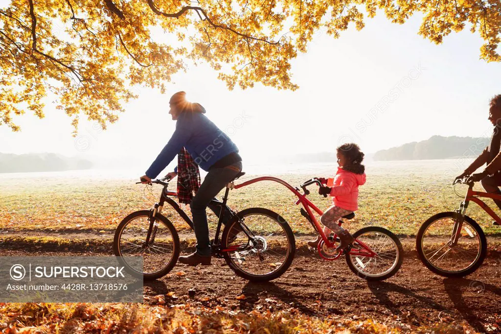 Father and daughter bike riding with trailer bike in sunny autumn park