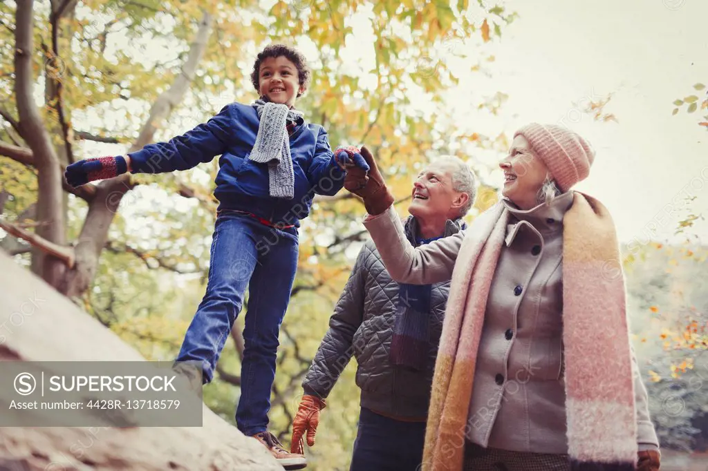 Grandparents walking grandson on log in autumn park