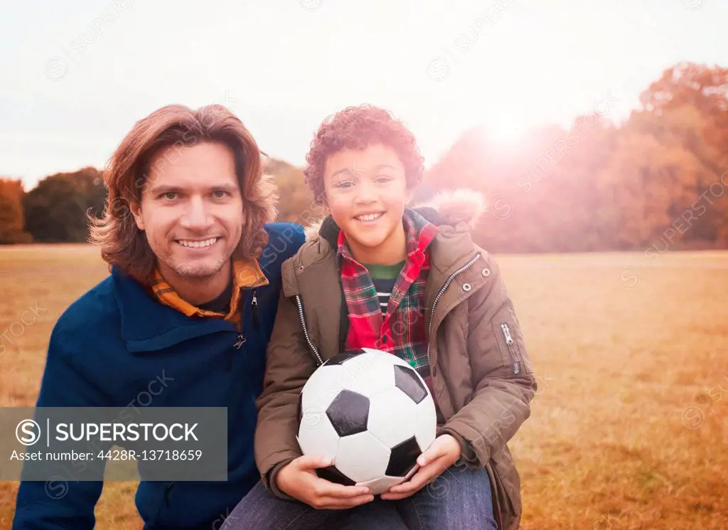 Portrait smiling father and son with soccer ball in park grass
