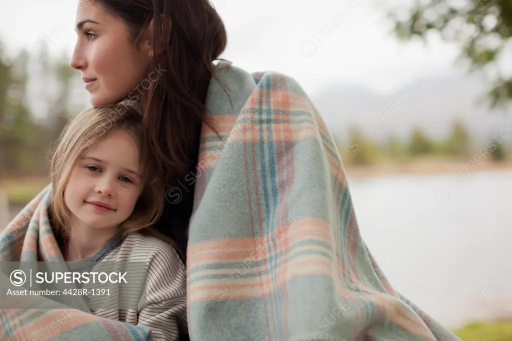 Cape Town, Portrait of smiling daughter wrapped in blanket with mother at lakeside