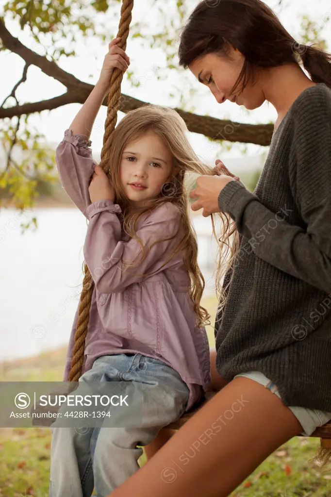 Cape Town, Mother braiding daughters hair on swing at lakeside