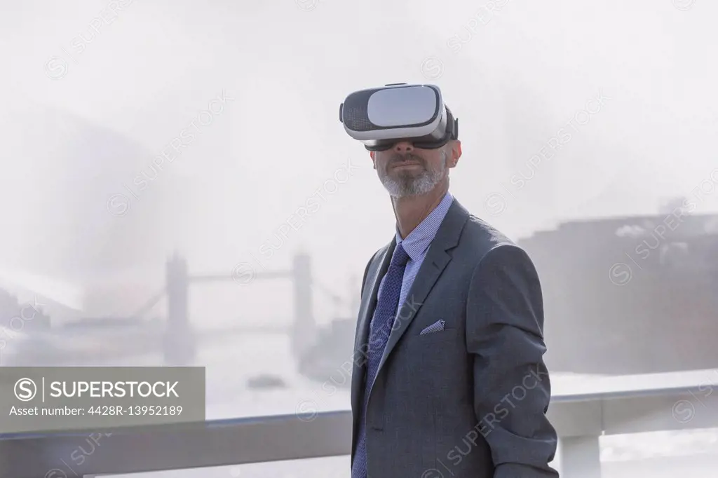 Businessman using virtual reality simulator glasses on sunny urban bridge over Thames River, London, UK