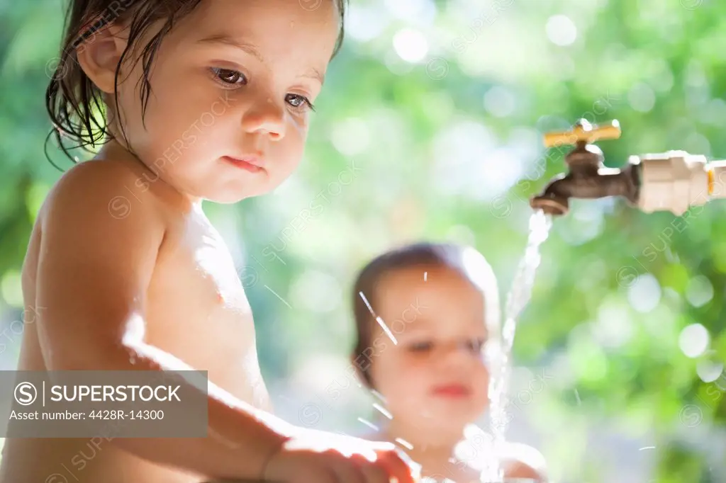 Baby girls playing in water spout outdoors, Mexico