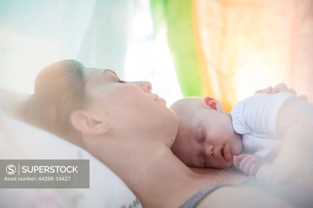 Mother and baby girl sleeping on bed, London, UK