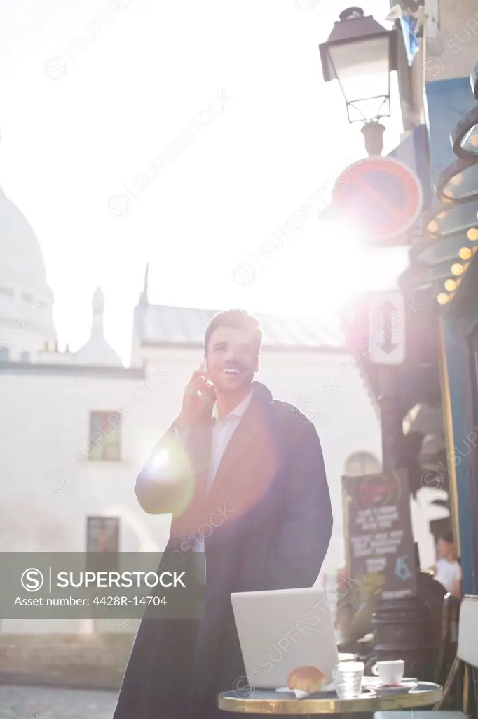 Businessman talking on cell phone at sidewalk cafe, Paris, France