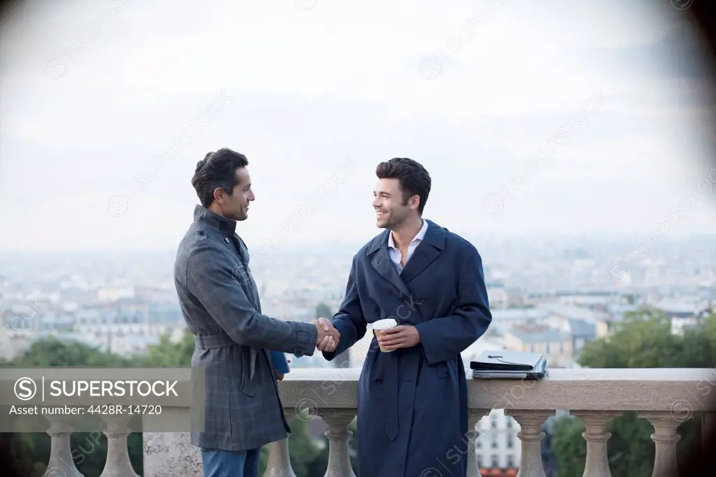 Businessmen shaking hands at railing overlooking Paris, France, Paris, France