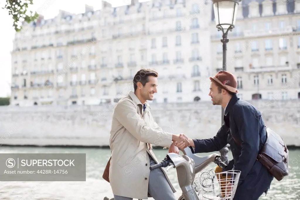 Businessmen handshaking on bicycles along Seine River, Paris, France, Paris, France