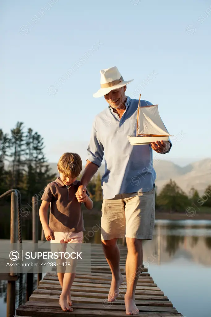 Cape Town, Grandfather and grandson with toy sailboat walking along dock over lake