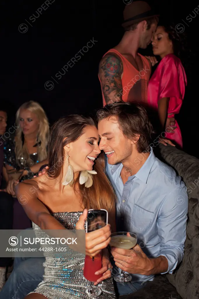 Cape Town, Smiling couple drinking cocktails and taking self-portrait with camera phone in nightclub