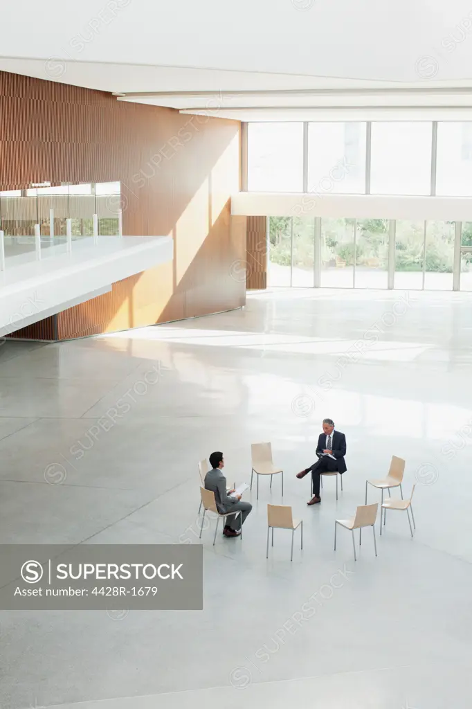 Spain, Businessmen sitting at circle of chairs in modern lobby