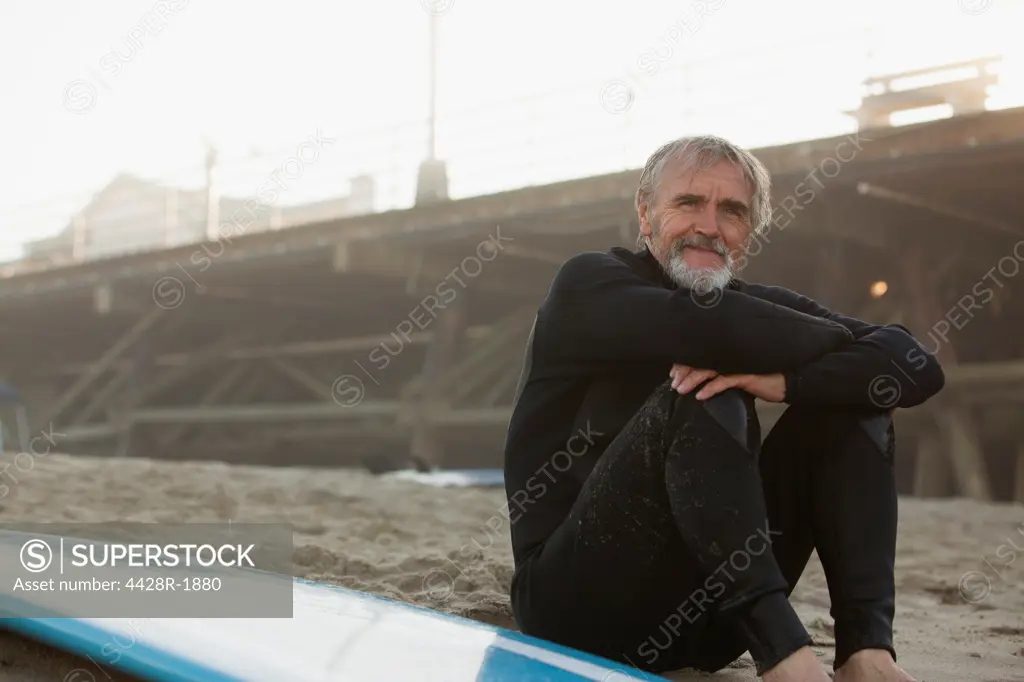 Los Angeles, USA, Older surfer sitting with board on beach