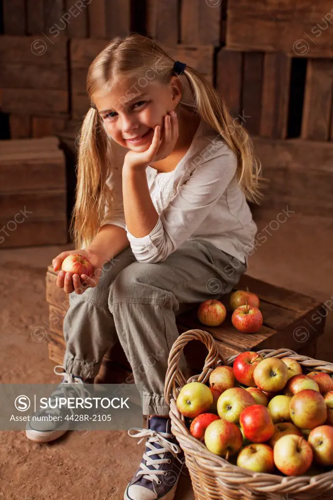 Cape Town, South Africa, Portrait of smiling girl sitting next to bushel of apples in barn