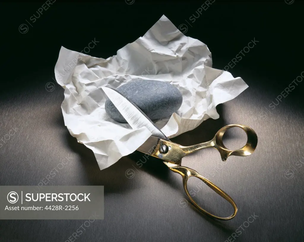 Scissors cutting into paper with rock