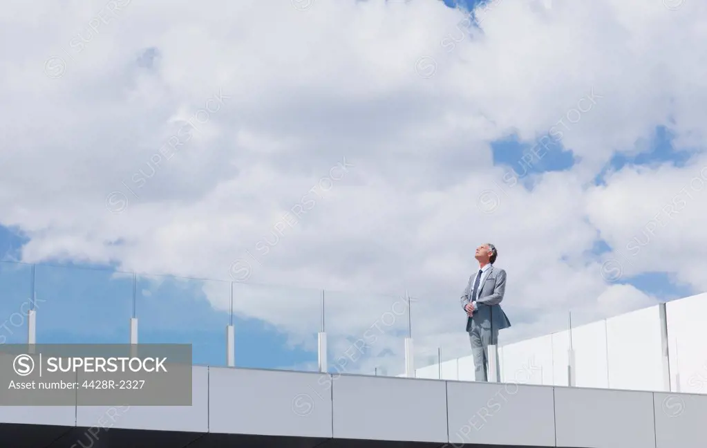 Spain, Pensive businessman looking up at sky on rooftop balcony
