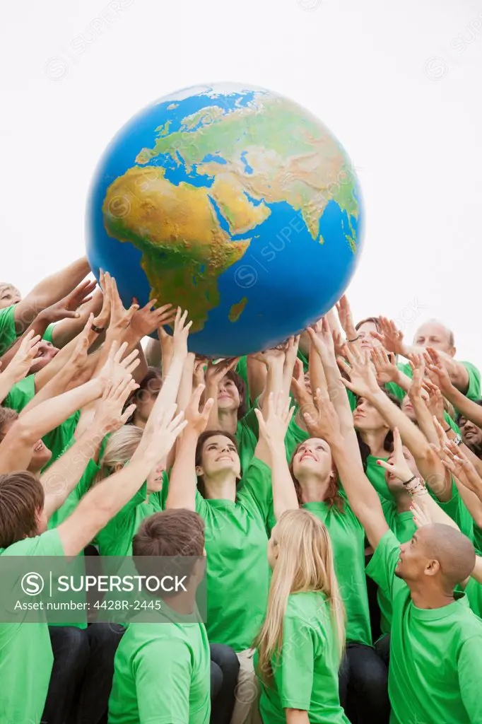 Cape Town, South Africa, Team in green t-shirts reaching for globe overhead