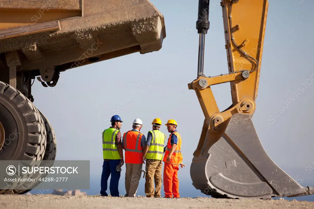 Workers talking by machinery in quarry, Spain