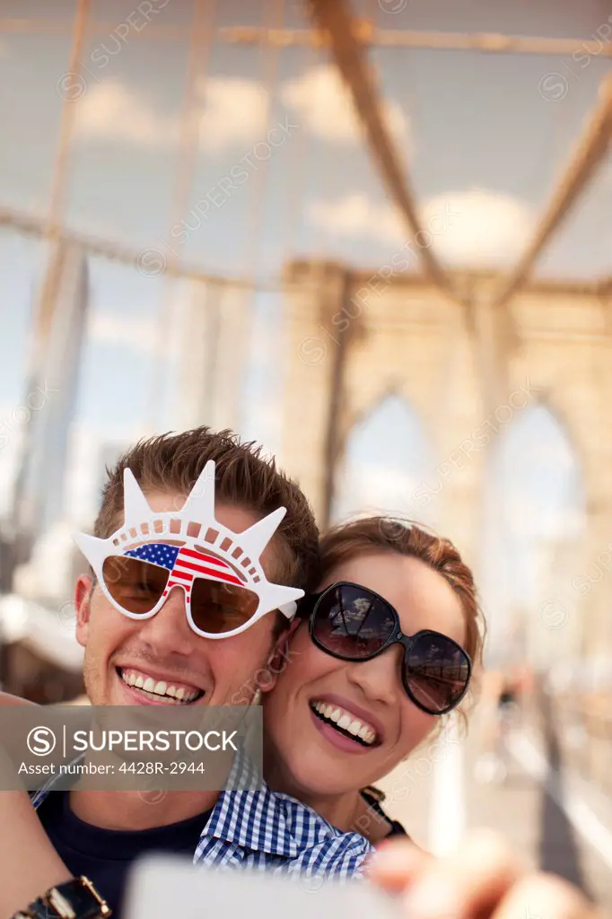 Couple in novelty sunglasses taking picture on urban bridge,New York