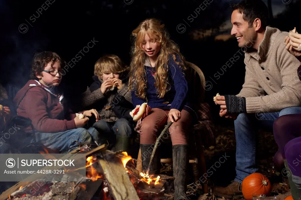 Family eating around campfire at night,belmonthouse, UK