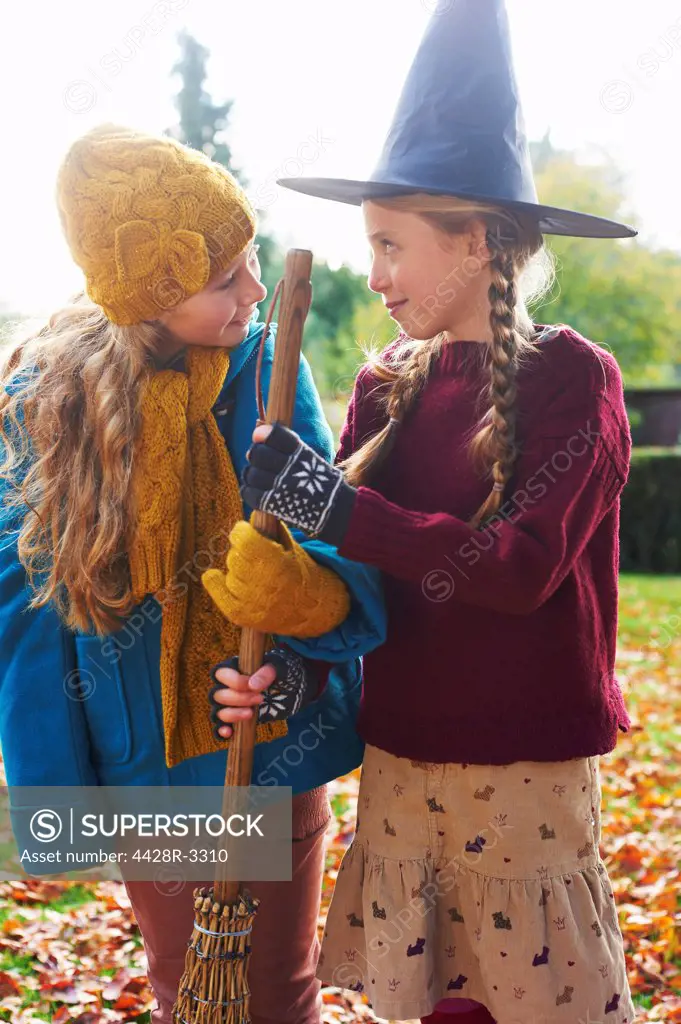 Girls playing with witch's hat and broom outdoors,belmonthouse, UK