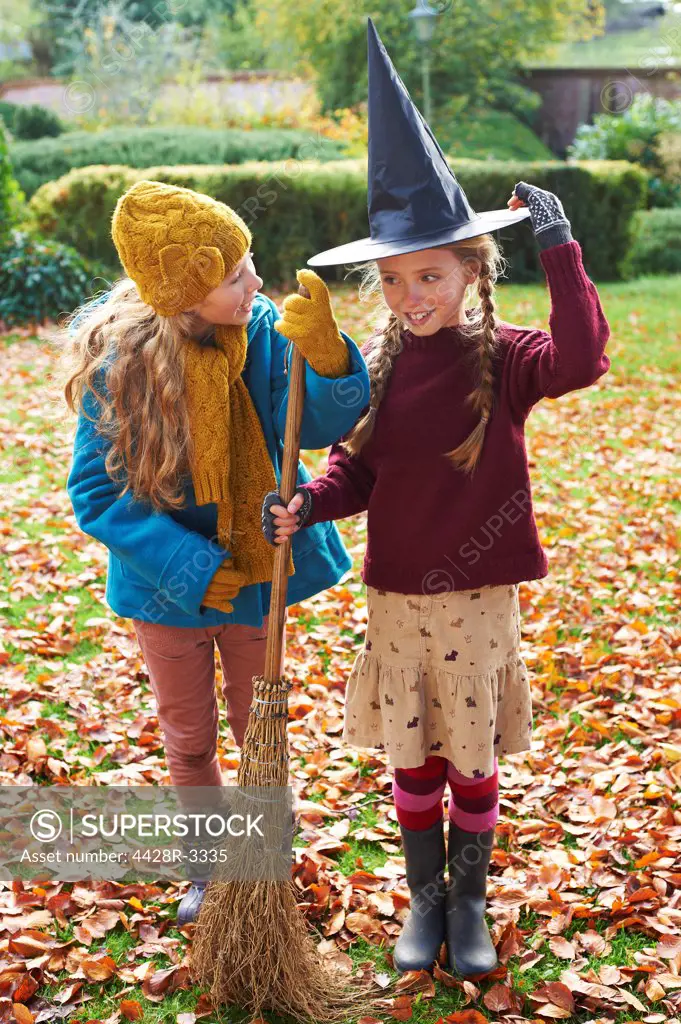 Girls playing with witch's hat and broom outdoors,belmonthouse, UK