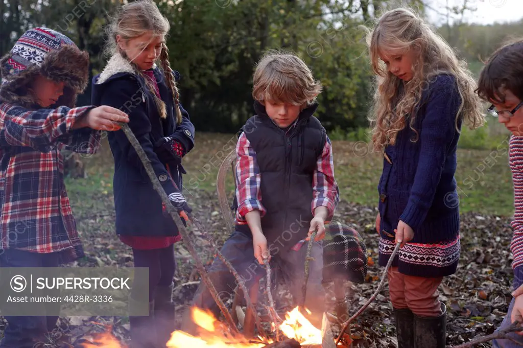Children poking bonfire outdoors,belmonthouse, UK