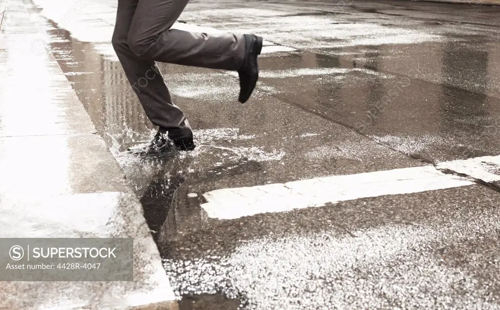 Businessman stepping in puddle on city street,New York