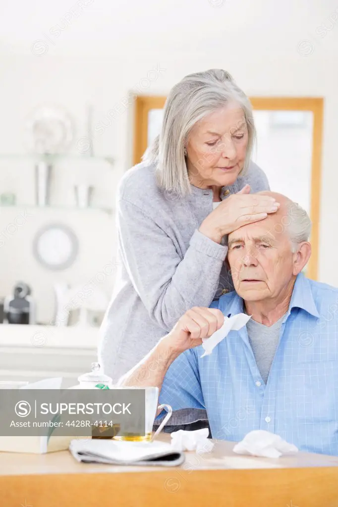 Older woman feeling sick husband's forehead,East Grinstead, UK