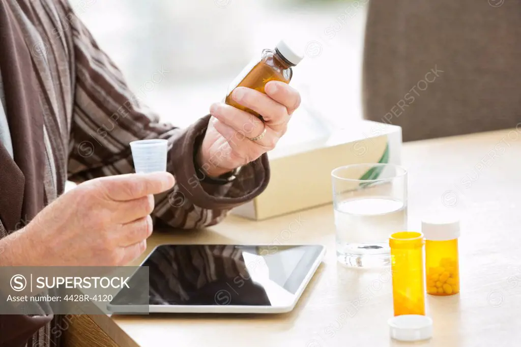 Older man taking medications at table,East Grinstead, UK