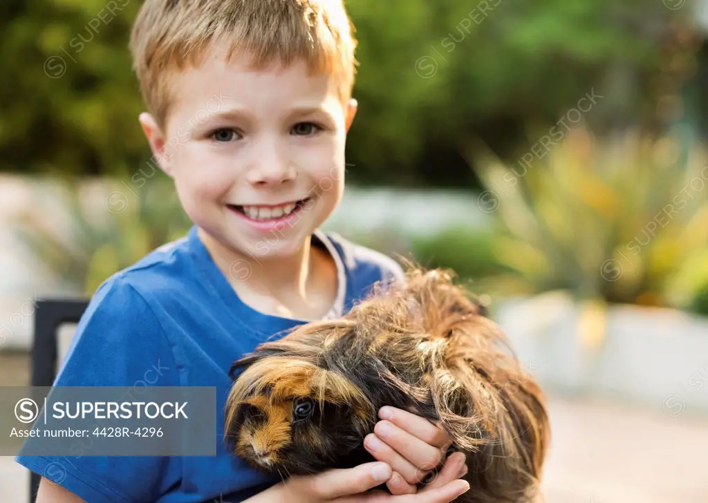 Smiling boy holding guinea pig outdoors,Guildford, UK