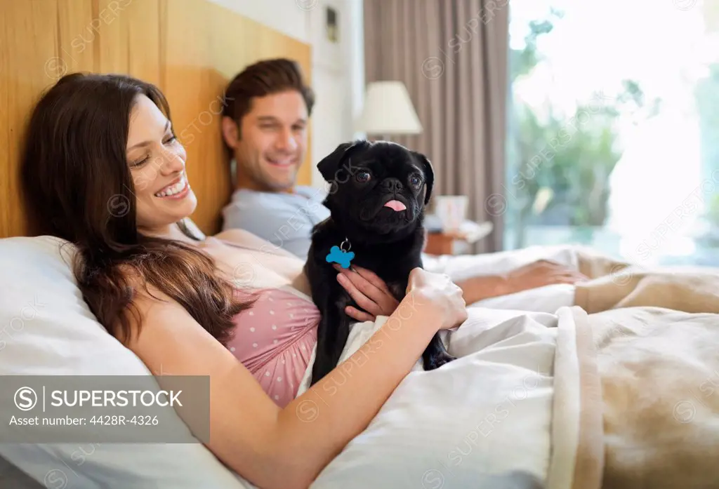 Couple relaxing with dog in bed,Guildford, UK