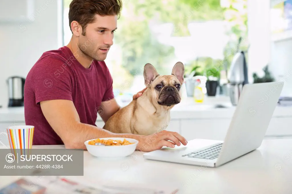 Man on laptop petting dog in kitchen,Guildford, UK
