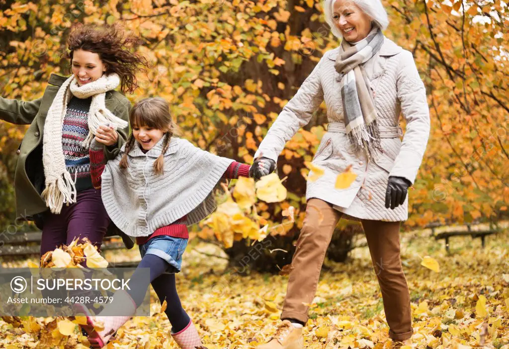 Three generations of women playing in autumn leaves,London, UK