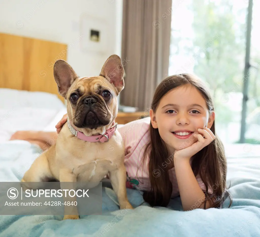 Smiling girl relaxing with dog on bed,Guildford, UK